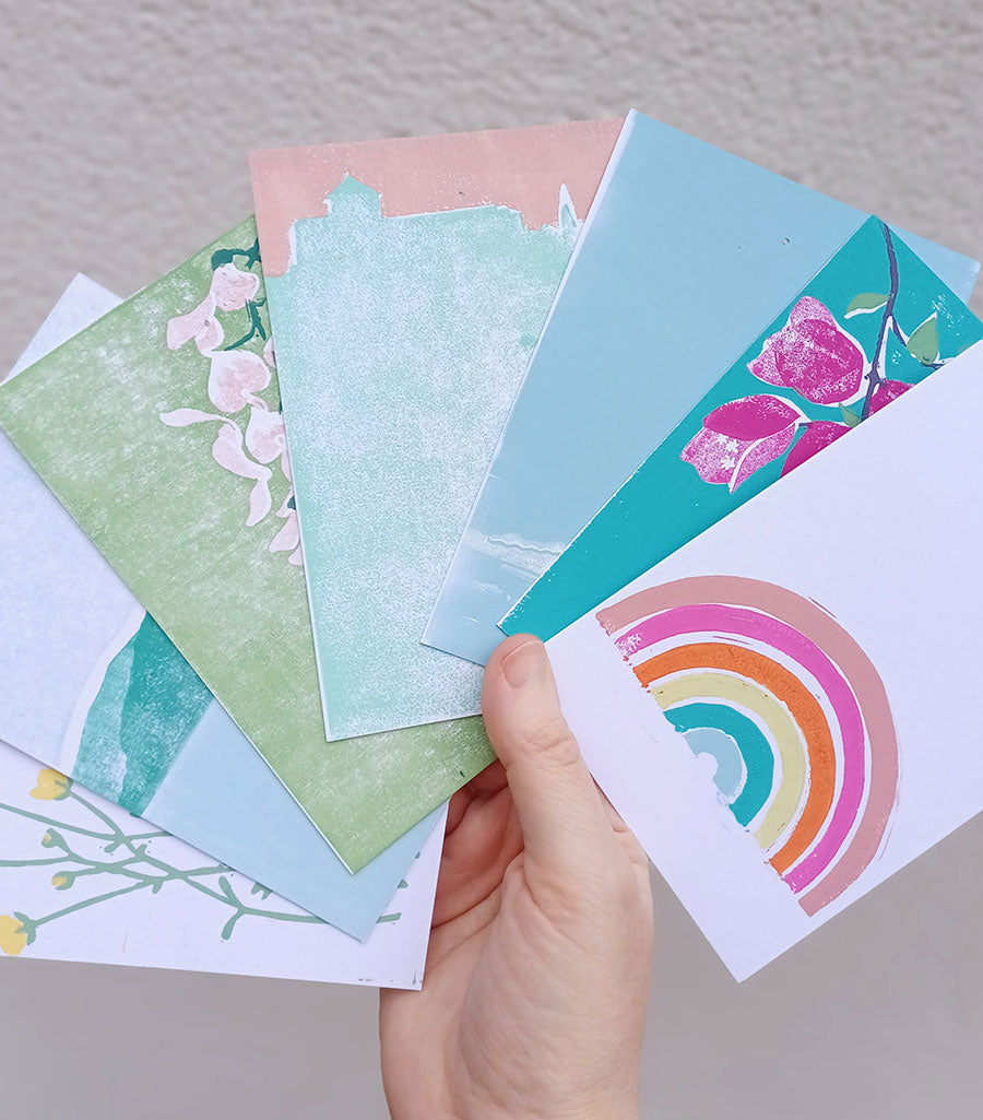 Hand holding a stack of colorful greeting cards with floral and rainbow designs.