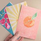 Three colorful greeting cards with different designs held by a hand on a beige background