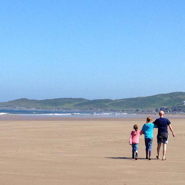 family walking arm in arm along an empty beach in England